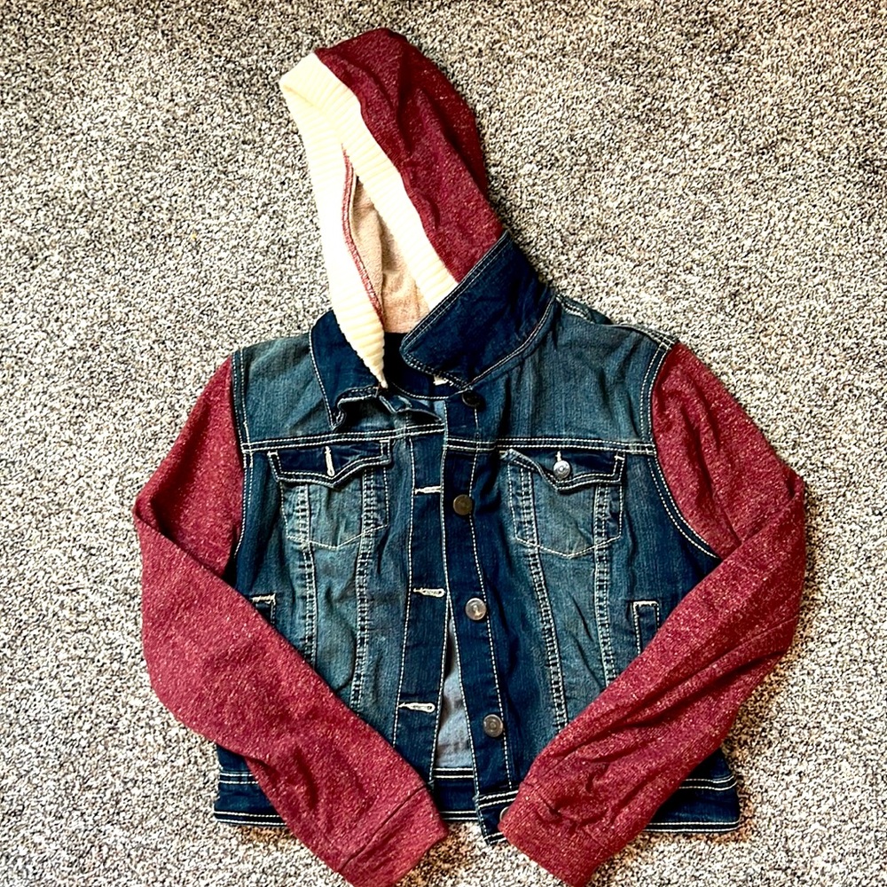 A warm and fashionable jean jacket with cloth arms and a hoodie.